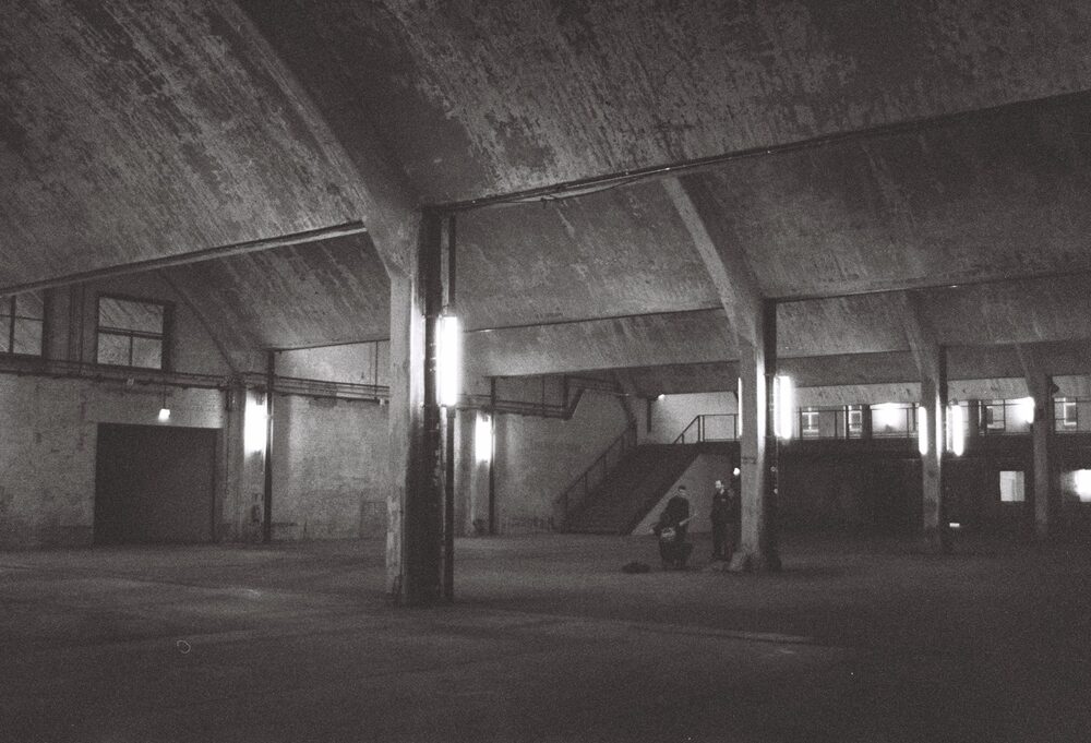 Monom, two people by the stairwell in the empty warehouse